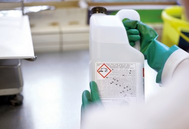 Eine Person mit Schutzhandschuhen schaut sich einen Behälter mit Gefahrstoffkennzeichen an.