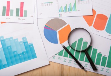 Mehrere ausgedruckte Diagramme (Balken- und Kreisdiagramme) auf einem Tisch, darauf eine Lupe und ein Stift zur Analyse von Daten. (Bild: tonefotografia - stock.adobe.com)