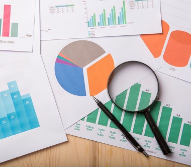 Mehrere ausgedruckte Diagramme (Balken- und Kreisdiagramme) auf einem Tisch, darauf eine Lupe und ein Stift zur Analyse von Daten. (Bild: tonefotografia - stock.adobe.com)